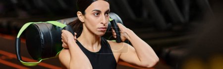 beautiful athletic woman with brunette hair exercising actively with power bag in gym, banner