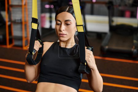 Photo for Appealing sporty woman with brunette hair in comfy sportwear using pull ups equipment in gym - Royalty Free Image