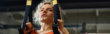 Photo for Good looking woman in comfortable sportwear exercising with pull ups equipment while in gym, banner - Royalty Free Image
