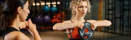 Photo for Beautiful sporty female coach in sportwear explaining how to use weight plate to her client, banner - Royalty Free Image