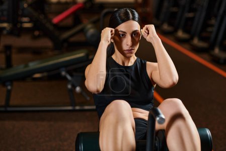 atlética mujer guapa con cabello moreno en cómoda prensa de bombeo de ropa deportiva mientras está en el gimnasio