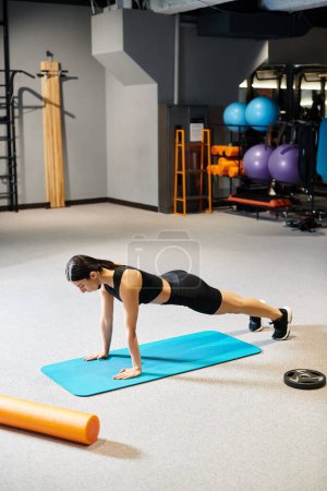 attraktive Frau mit dunklen Haaren in schwarzer Sportbekleidung, die sich im Fitnessstudio aktiv auf der Fitnessmatte dehnt