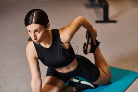 attraktive athletische Frau in schwarzer Sportbekleidung, die im Fitnessstudio ihre Muskeln auf der Fitnessmatte dehnt