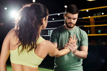 Téléchargez les photos : Un entraîneur masculin enseigne des techniques d'auto-défense à une femme dans un cadre de gymnastique, car ils se tiennent côte à côte. - en image libre de droit