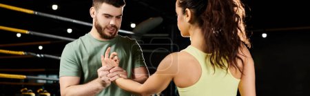 Un entraîneur masculin démontre des techniques d'auto-défense à une femme dans un environnement de gymnase.