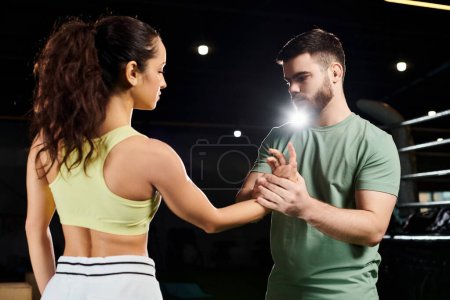 A male trainer demonstrates self-defense techniques to a woman in a gym.