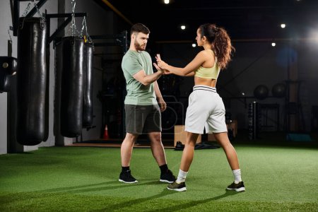 Un entrenador masculino demuestra técnicas de autodefensa a una mujer en un gimnasio, mostrando fuerza y empoderamiento.