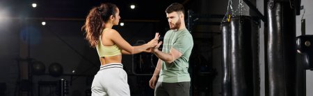 Foto de Entrenador de fitness masculino mostrando técnicas de autodefensa a una mujer en un gimnasio, enfocado y comprometido. - Imagen libre de derechos