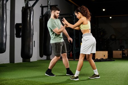 A male trainer is teaching self-defense techniques to a woman in a gym setting.