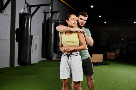 A male trainer teaches self-defense techniques to a woman in a gym, focusing on strength and empowerment.