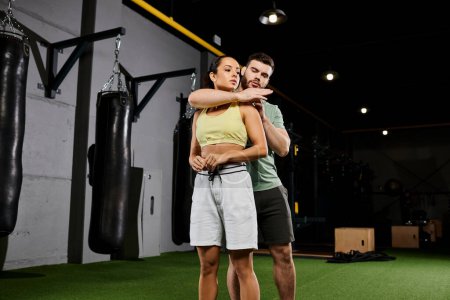 A male trainer guides a woman in mastering self-defense techniques in a gym, showcasing strength and empowerment.