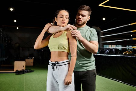 A male trainer is demonstrating self-defense techniques to a woman in a gym setting.