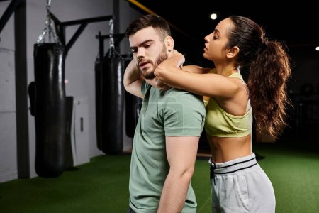 A male trainer demonstrates self-defense techniques to a woman in a well-equipped gym setting.