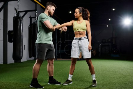 A male trainer demonstrates self-defense techniques to a woman in a gym setting.