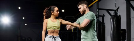 Un entrenador masculino demuestra técnicas de autodefensa a una mujer en un entorno de gimnasio.