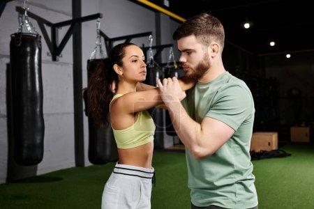 A male trainer guiding a woman through self-defense techniques in a gym.
