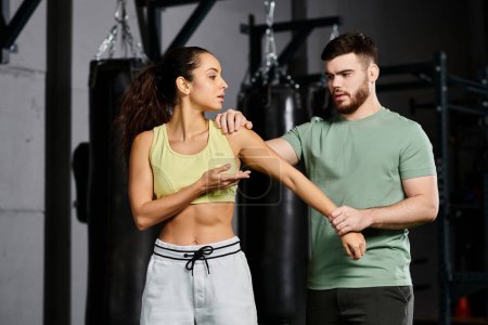 A male trainer demonstrates self-defense techniques to a woman in a gym setting, focusing on fitness and strength.
