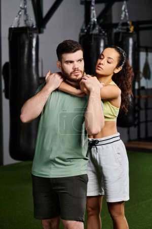 Un entrenador masculino demuestra técnicas de autodefensa a una mujer en un gimnasio, fomentando el empoderamiento y la unidad.