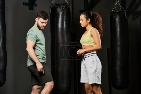 Un entraîneur masculin enseigne des techniques d'auto-défense à une femme dans une salle de gym.