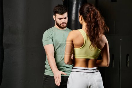 A male trainer demonstrates self-defense techniques to a woman in a gym setting.