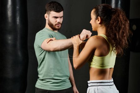 A male trainer teaches self-defense techniques to a woman in a gym setting.