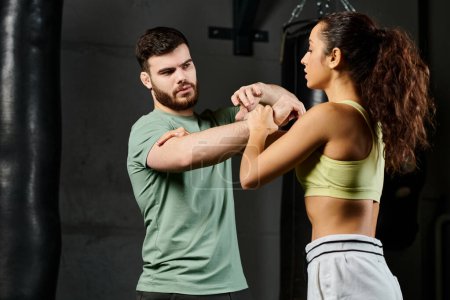 A male trainer demonstrates self-defense techniques to a woman in a gym.