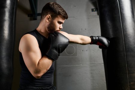 Hombre barbudo guapo con camiseta negra y guantes de boxeo golpea ferozmente una bolsa en un gimnasio.