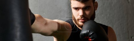 A handsome man with a rugged beard wearing boxing gloves punches a bag in the gym with determination and skill.