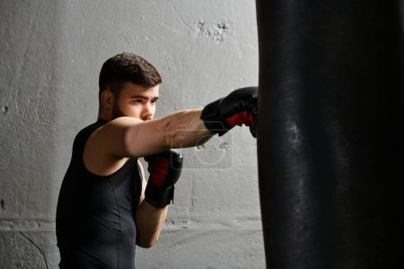 A handsome man with a beard wearing a black shirt and black boxing gloves, punching a bag in a gym.