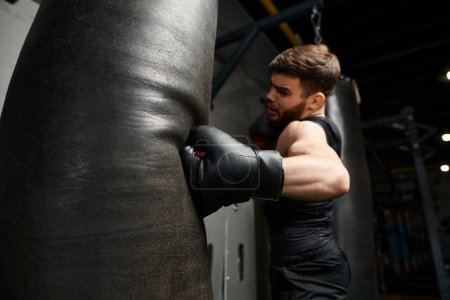 A man with a beard wearing a black shirt and boxing gloves, fiercely punching a bag in a gym.