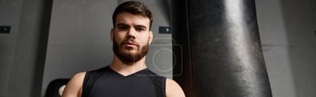 Un bel homme avec une barbe boxe à côté d'un sac de boxe dans une salle de gym.