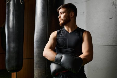 Un hombre barbudo con una camiseta negra y guantes de boxeo golpea una bolsa en un gimnasio.