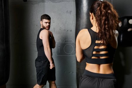 Ein männlicher Trainer unterstützt eine entschlossene brünette Sportlerin beim Boxtraining in einem Fitnessstudio.