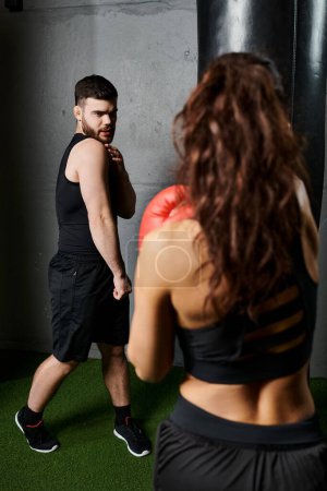 A male trainer coaches a brunette sportswoman in active wear during a boxing session in the gym.