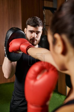 A woman in a black shirt and red boxing gloves practices boxing in a gym.