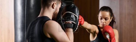 Un entrenador masculino está al lado de una deportista morena en ropa activa, que está boxeando en un gimnasio.