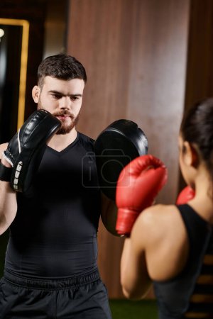 Téléchargez les photos : Un homme en chemise noire et gants de boxe rouges se prépare pour un match dans un cadre de gymnastique. - en image libre de droit