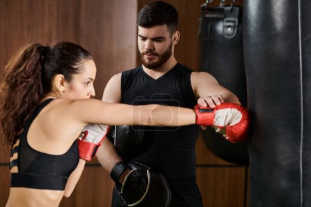 A male trainer stands beside a brunette sportswoman wearing boxing gloves, actively training in a gym.