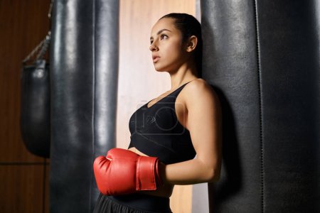 Eine brünette Sportlerin zeigt Power und Kraftboxen in einem Fitnessstudio, trägt ein schwarzes Oberteil und leuchtend rote Boxhandschuhe.