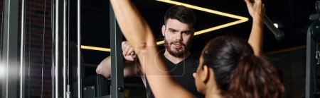Téléchargez les photos : Un entraîneur masculin se tient aux côtés d'une sportive brune alors qu'ils s'observent dans un miroir de gymnase. - en image libre de droit