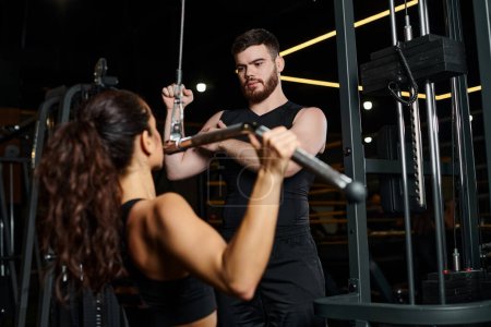 Ein männlicher Trainer führt eine brünette Sportlerin durch ein Workout in einem Fitnessstudio und konzentriert sich dabei auf Kraft und Fitness.