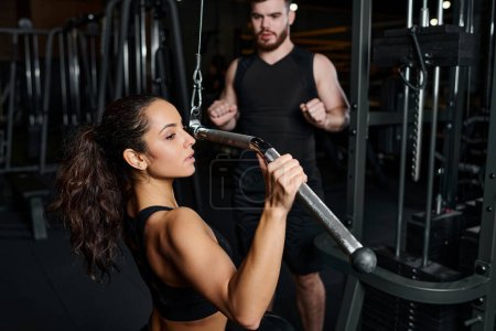 A male trainer and a brunette sportswoman are seen working out together in a gym, focused and determined.