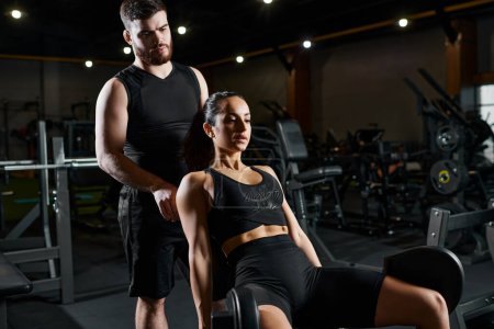 Photo for A male trainer stands next to a brunette sportswoman in a gym, assisting with a workout routine. - Royalty Free Image