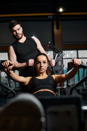 Téléchargez les photos : Un entraîneur masculin assiste une sportive brune avec des exercices dans une salle de gym. - en image libre de droit