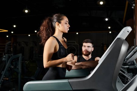 Photo for A male personal trainer and a brunette sportswoman running energetically on a treadmill in a gym. - Royalty Free Image