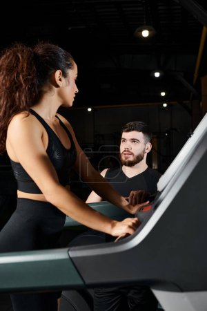Un entrenador personal masculino ayuda a una deportista morena en una cinta de correr en un gimnasio.