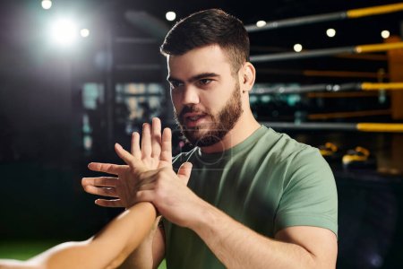 A man demonstrates self-defense techniques to a woman in a gym setting in front of a camera.