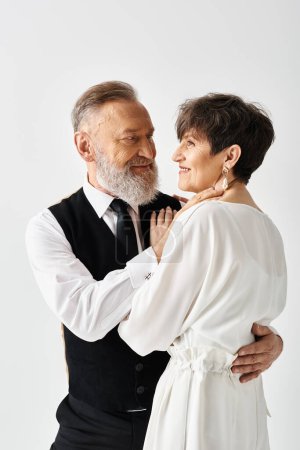 A middle-aged bride and groom in wedding gowns embrace, celebrating their special day in a studio setting.