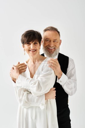 Middle aged bride and groom in wedding gowns standing together in studio, celebrating their special day.