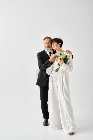 Téléchargez les photos : Mariée d'âge moyen et marié en robes de mariée posant gracieusement ensemble dans un cadre de studio sur leur jour spécial. - en image libre de droit